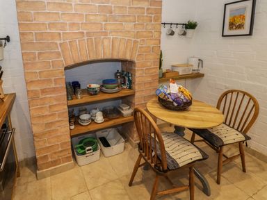 A small dining area with a round wooden table and two wooden chairs with cushions next to shelves inside a brick alcove with dishes and glassware at The Escape in Malvern