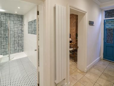 A hallway with tiled floor leading to a bathroom and a kitchen with brick walls at The Escape in Malvern