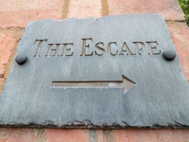 A directional stone sign with the words The Escape and an arrow on a brick wall at The Escape in Malvern