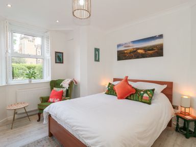 A bedroom with a bed pillows a green armchair a small table and window at The Escape in Malvern
