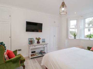 A bedroom with a bed green armchairs a wall-mounted tv and white cabinets at The Escape in Malvern