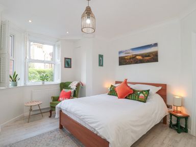 A bedroom with a bed a green armchair plants and wall pictures at The Escape in Malvern