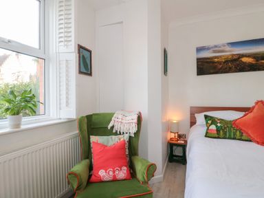 A bedroom with a green armchair and decorated bed near a window with a plant at The Escape in Malvern