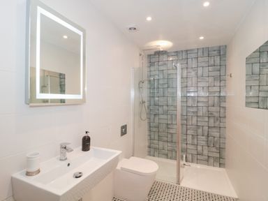 A bathroom with a wall-mounted sink toilet and shower area with patterned tiles at The Escape in Malvern