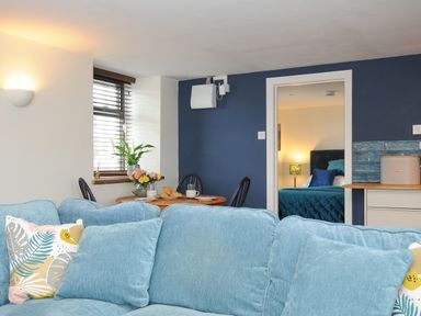 A living room with a blue sofa and a dining table with flowers and croissants at The Bower in Manaccan near St Keverne