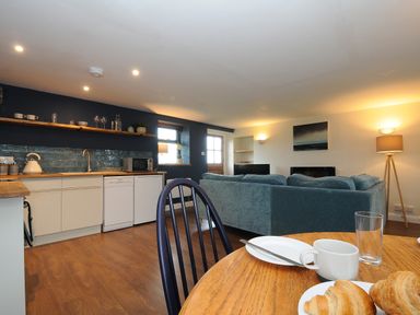 An open plan kitchen and living area with a round wooden table with dishes and croissants at The Bower in Manaccan near St Keverne