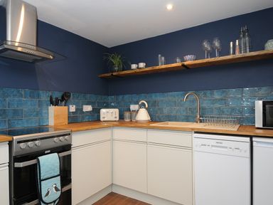 A kitchen with white cabinets blue tiled backsplash wooden countertop and stainless steel stove at The Bower in Manaccan near St Keverne