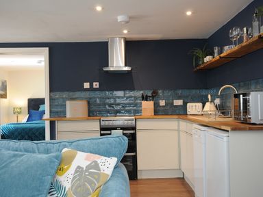 A kitchen with wooden countertops and white cabinets next to a blue sofa with patterned cushions at The Bower in Manaccan near St Keverne