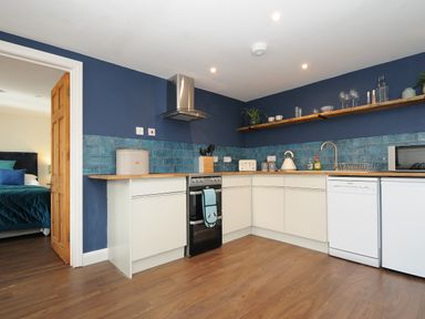 A kitchen with white cabinets blue tiled backsplash wooden countertops and appliances at The Bower in Manaccan near St Keverne