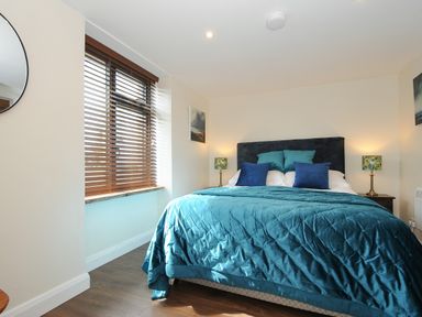 A bedroom with a bed with teal and blue bedding and pillows two bedside tables and lamps wooden blinds on the window at The Bower in Manaccan near St Keverne