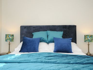 A bed with blue and teal pillows and blanket with two bedside lamps with peacock patterned shades at The Bower in Manaccan near St Keverne