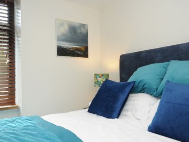 A bedroom with a bed with blue and teal pillows and a painting on the wall at The Bower in Manaccan near St Keverne