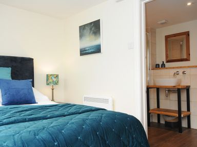 A bedroom with a bed blue pillows and a blue comforter with a bathroom visible through an open door at The Bower in Manaccan near St Keverne