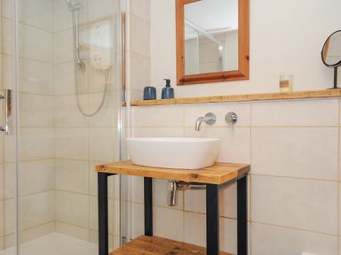 A bathroom with a shower enclosure and a wooden sink stand with a white sink and mirror at The Bower in Manaccan near St Keverne