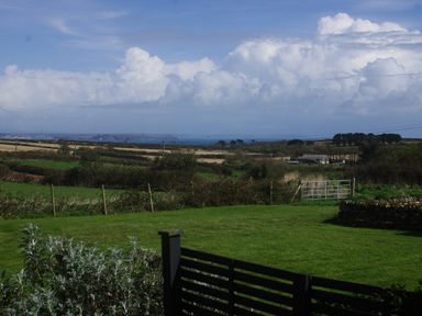A grassy garden with bushes wooden fence and metal gate overlooking fields and distant coastline at The Bower in Manaccan near St Keverne