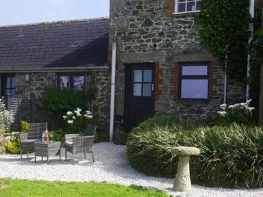 An outdoor seating area with two chairs and a table on a gravel area in front of a stone house at The Bower in Manaccan near St Keverne