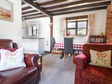 A living room with armchairs a dining table with checkered tablecloth and a kitchen in the background at Coach Cottage in Colyton