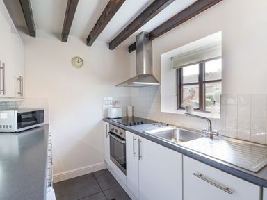 A kitchen with white cabinets a microwave oven a stove and a sink under a window at Coach Cottage in Colyton