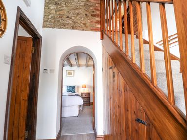 A hallway with wooden staircase and stone wall leading to a bedroom at Coach Cottage in Colyton