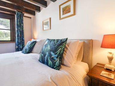 A bedroom with a bed white sheets blue patterned pillows a wooden nightstand with a lamp and framed pictures on the wall at Coach Cottage in Colyton