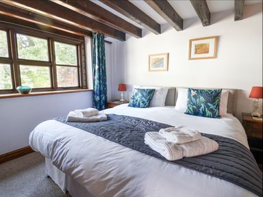 A bedroom with a large bed towels on the bed two bedside tables and a window with curtains at Coach Cottage in Colyton