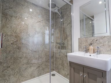 A shower with a glass door next to a sink with a mirror above it in a bathroom at Coach Cottage in Colyton