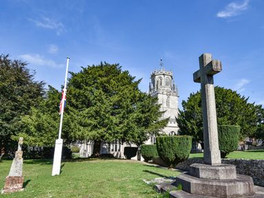 A church tower with large trees and a stone cross in the foreground at Coach Cottage in Colyton