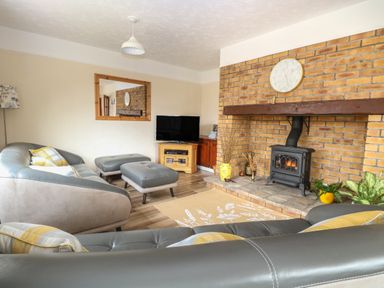 A living room with a brick fireplace a clock on the mantel a television a sofa ottomans and a rug at Dove's Nest in Martham