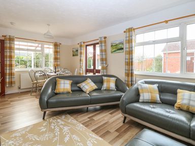 A living room with two gray sofas with plaid cushions and a dining table with chairs near windows at Doves Nest in Martham