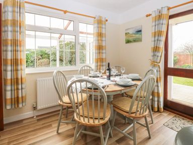 A dining area with a round wooden table set for six and chairs near windows and a door at Doves Nest in Martham