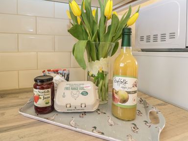 A kitchen tray with a jar of Norfolk strawberry jam a carton of free range eggs a bottle of Suffolk apple juice and a vase of yellow tulips at Dove's Nest in Martham