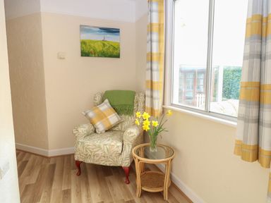A corner with a patterned armchair a side table with flowers curtains and a painting on the wall at Doves Nest in Martham