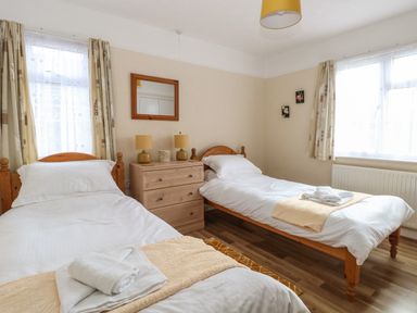 A bedroom with two single beds a dresser with two lamps and two windows at Dove's Nest in Martham