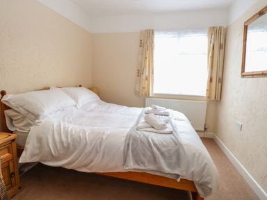 A bedroom with a double bed white bedding towels on bed a window with curtains and a wooden mirror on the wall at Dove's Nest in Martham