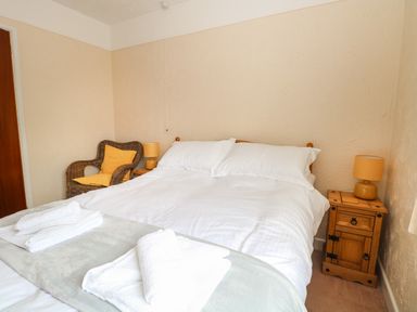 A bedroom with a double bed white linens bedside tables lamps and a wicker chair at Dove's Nest in Martham