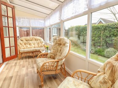 A sunroom with wicker chairs and sofa with cushions and a small table with flowers at Doves Nest in Martham