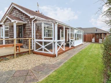 A house with a wooden deck and a glass enclosed porch next to a grassy yard and a wooden shed at Dove's Nest in Martham