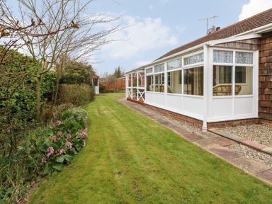 A garden with green grass flower beds and a white conservatory attached to a house at Doves Nest in Martham