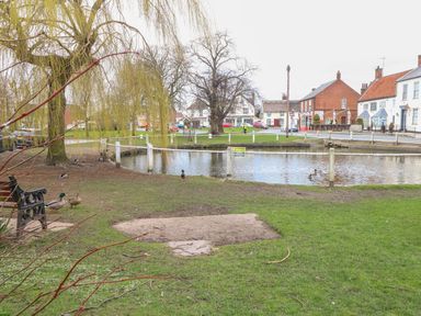 A park with a pond ducks bench and houses in the background at Doves Nest Martham