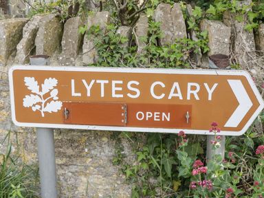 A brown arrow sign with white text and oak leaf symbol pointing to Lytes Cary with flowers and ivy around it at Garden View in Wellington