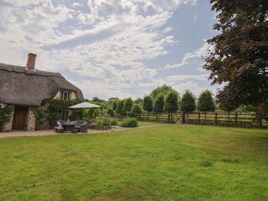 A thatched roof house with outdoor seating and trees at Garden View in Wellington