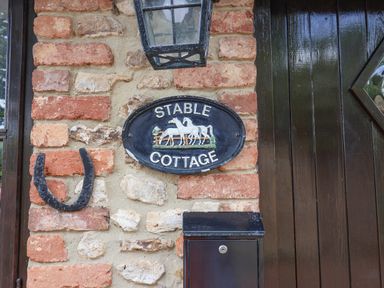 A brick wall with a horseshoe a lamp a plaque reading Stable Cottage and a black mailbox next to a dark wooden door at Stable Cottage in Colyton