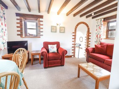A living room with red armchair and sofa wooden beams on ceiling and arched brick doorway at Stable Cottage in Colyton