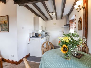 A kitchen and dining area with wooden chairs a table with flowers and kitchen appliances at Stable Cottage in Colyton