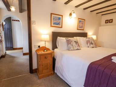 A bedroom with a bed with floral pillows bedside tables with lamps and a doorway at Stable Cottage in Colyton
