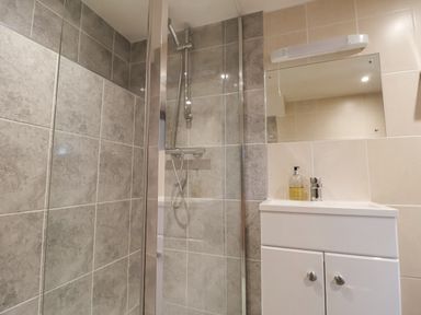 A bathroom with a tiled shower area and a white sink cabinet with a mirror above at Stable Cottage in Colyton