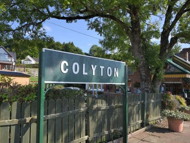 A green sign with the word Colyton in front of a wooden fence and trees at Stable Cottage in Colyton