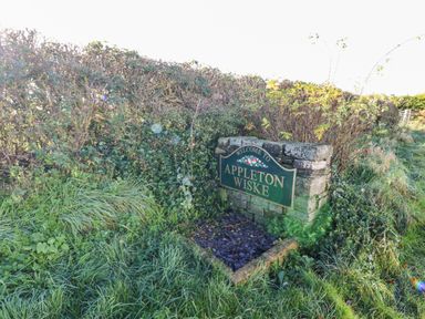 A stone sign with welcome to Appleton Wiske surrounded by grass and bushes at Anvil Cottage in Appleton Wiske