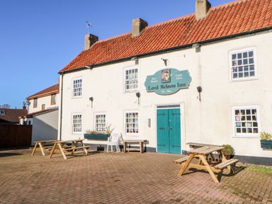 Exterior of a building with a tiled roof wooden picnic tables and a sign reading Lord Nelson Inn