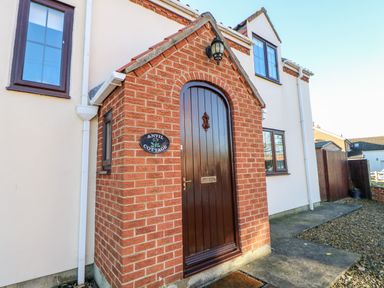 The front entrance of a house with a small brick porch and a wooden arched door at Anvil Cottage in Appleton Wiske